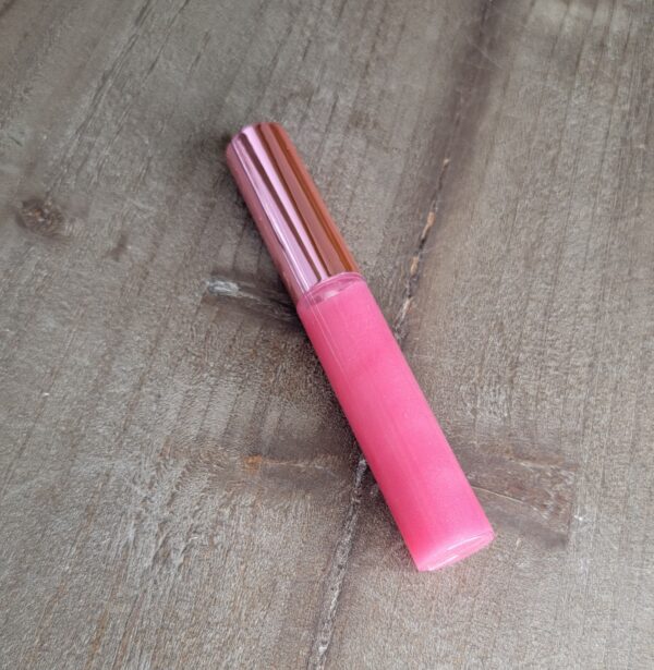 Pink lip gloss on wooden surface.