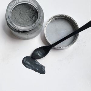 Gray powder in jar with black spatula.