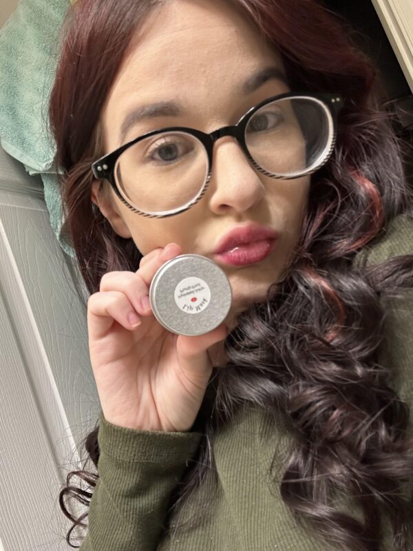 Woman holding lip balm with glasses on.